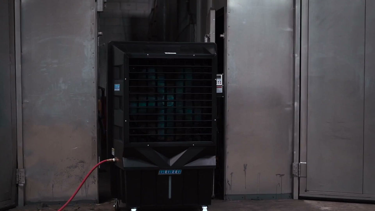 LEGACY-30 evaporative cooler between steel doors in an industrial bay, a red hose connected at its side