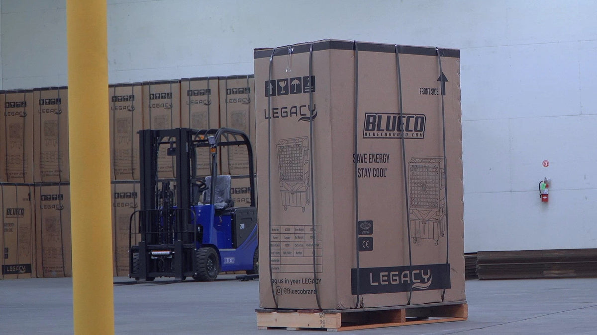A boxed LEGACY-30 evaporative cooler on a pallet in a BLUECO warehouse, more LEGACY cartons and an electric forklift behind