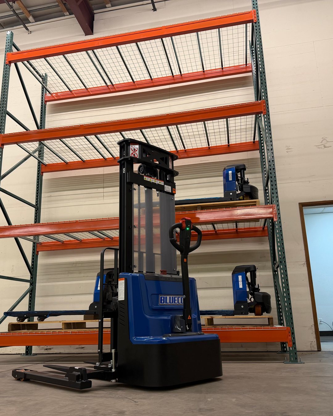 BLUECO straddle-leg stacker in front of orange warehouse racking