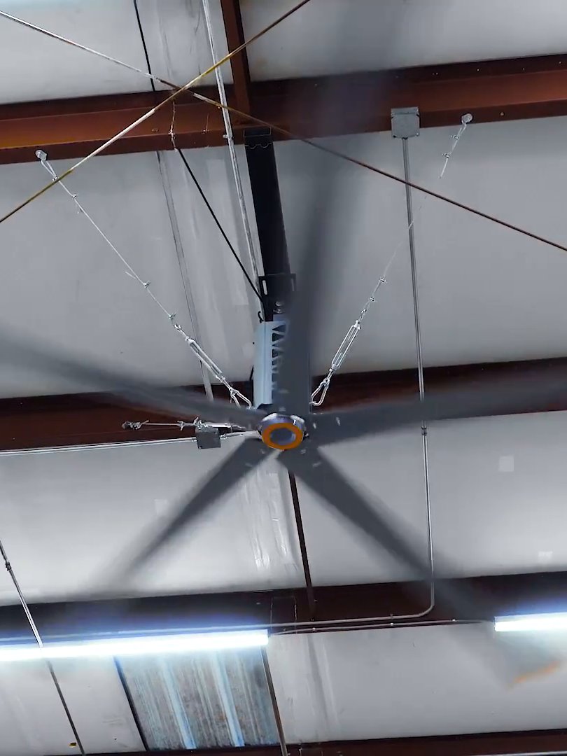 Eurus HVLS fan turning under a warehouse roof, its tension cables running out from the drive housing