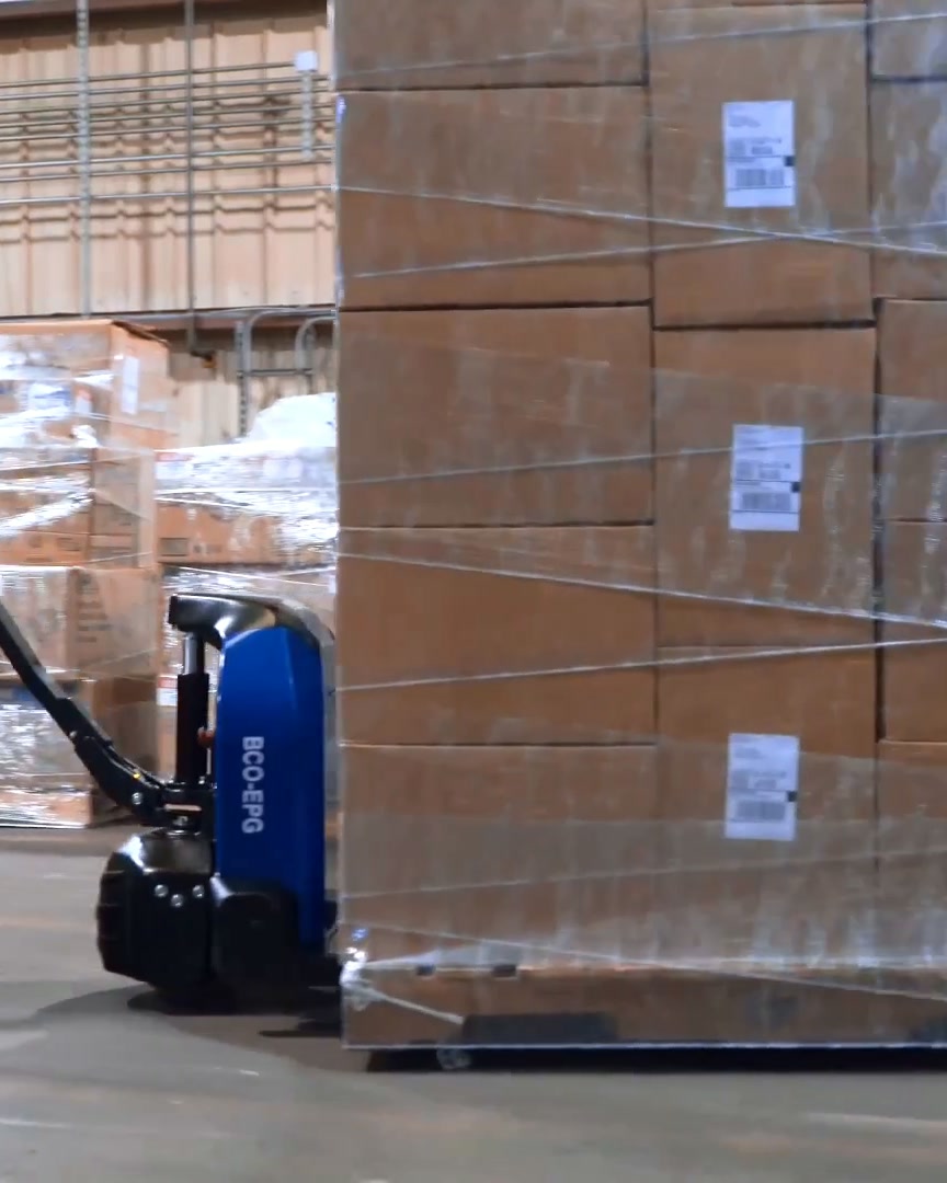 Electric pallet jack pulling a shrink-wrapped pallet of cartons across a warehouse floor
