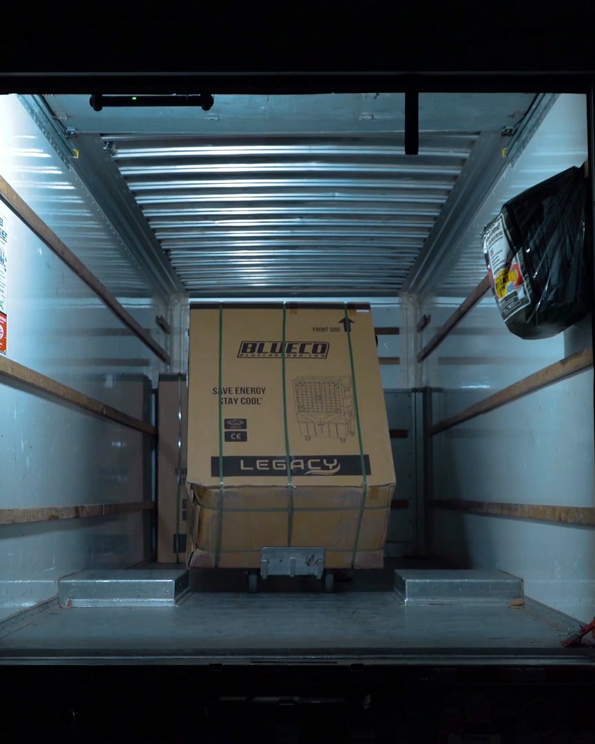 Box truck interior lit by a work light, with a boxed cooler inside